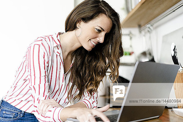 Lächelnde Frau benutzt Laptop in der Küche zu Hause
