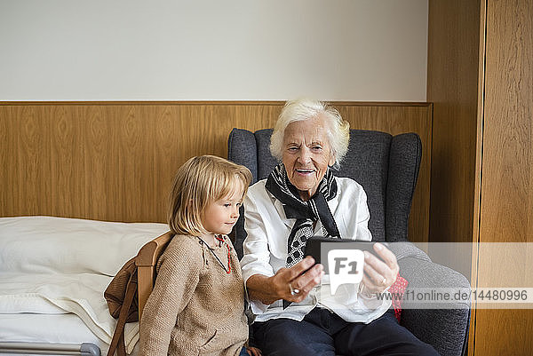 Porträt einer alten Frau  die zusammen mit ihrer Urenkelin Fotos auf einem Smartphone betrachtet