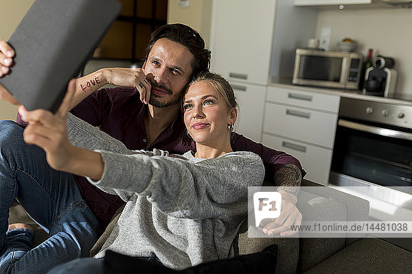 Paar  das im Wohnzimmer auf der Couch sitzt und mit seinem digitalen Tablet fotografiert