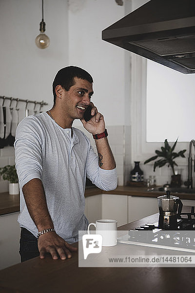 Lächelnder junger Mann am Handy in der heimischen Küche