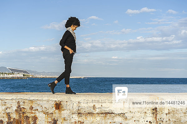 Spanien  Barcelona  lachende  schwarz gekleidete Frau  die bei Sonnenlicht an der Wand entlang geht