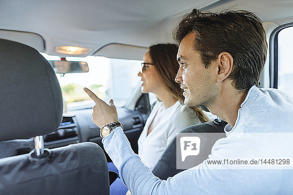 Ehepaar im Auto mit Frau auf dem Beifahrersitz und Mann  der vom Rücksitz aus mit dem Finger zeigt