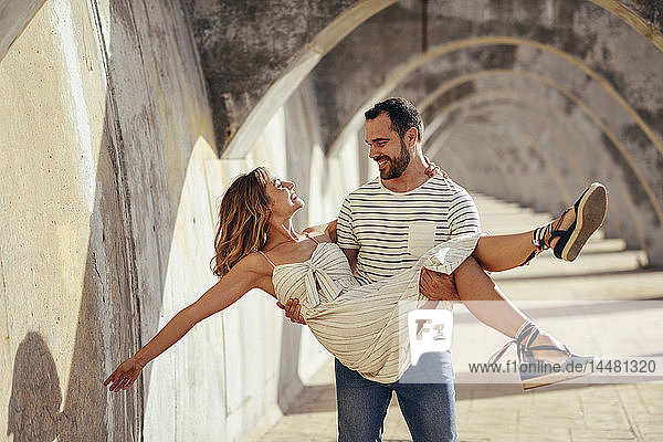 Spanien  Andalusien  Malaga  glücklicher Mann  der seine Freundin unter einem Torbogen in der Stadt trägt