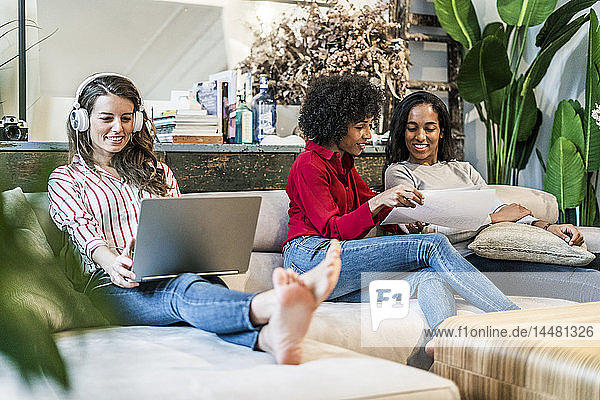 Three women with laptop and documents sitting on couch