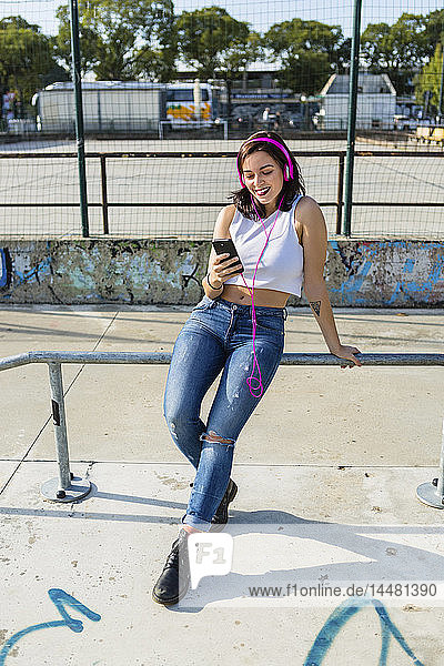 Lächelnde junge Frau mit Kopfhörer und Handy in der Stadt