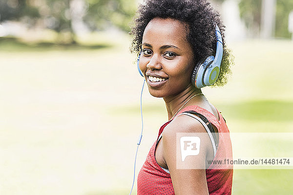 Porträt einer lächelnden  sportlichen jungen Frau mit Kopfhörern im Park