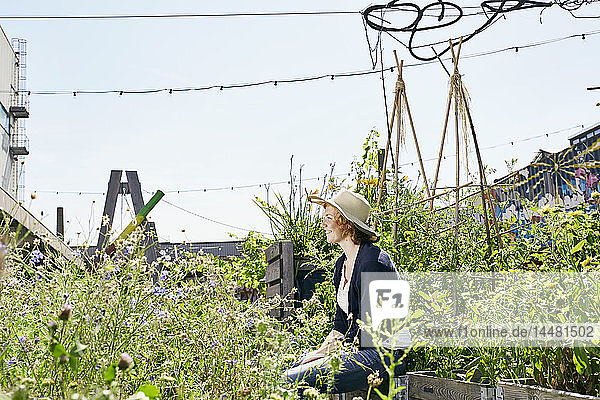 Lächelnde junge Frau mit Strohhut im Stadtgarten sitzend