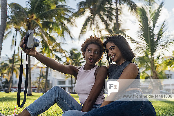 Two happy female friends taking an instant photo in a park