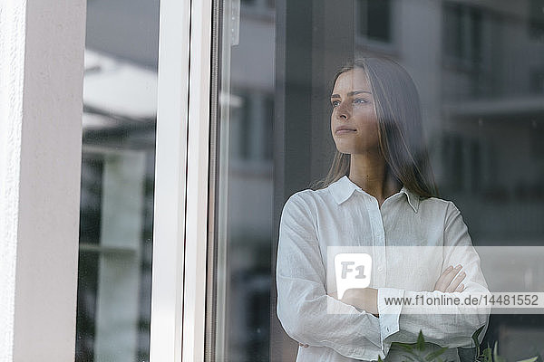 Junge Geschäftsfrau am Fenster stehend  mit verschränkten Armen
