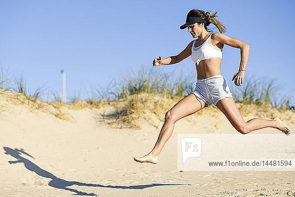 Sportliche Frau läuft am Strand entlang der Sanddünen