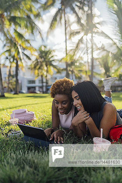 Zwei glückliche Freundinnen entspannen sich mit einer Tablette in einem Park