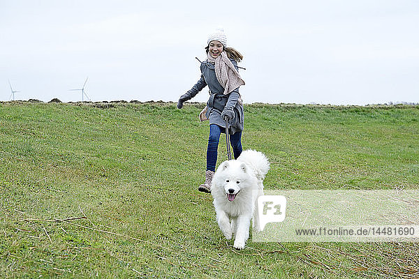Lachendes Mädchen rennt mit ihrem Hund auf einer Wiese