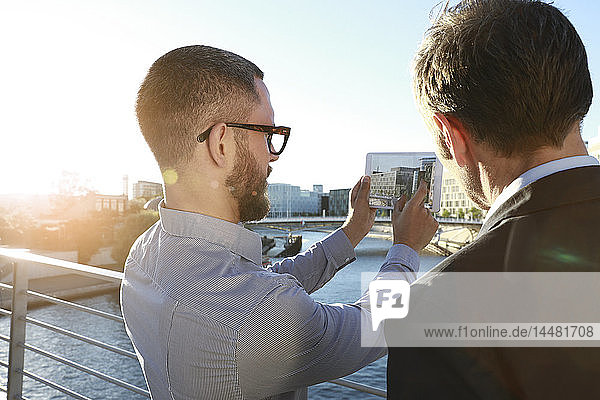 Zwei Geschäftsleute beim Fotografieren mit einer Tablette auf einer Brücke in der Stadt