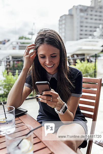 Junge schöne Frau benutzt ihr Smartphone auf einer Terrasse