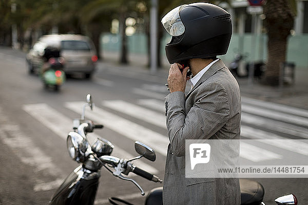 Businessman next to motorscooter putting on helmet