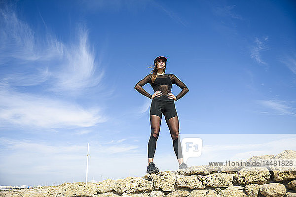 Selbstbewusste sportliche Frau auf Steinmauer stehend