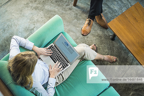 Top view of businesswoman working on laptop on turquoise couch in coworking space