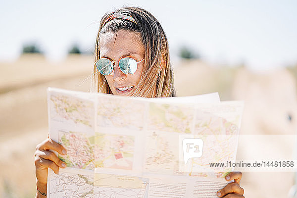 Blonde junge Frau mit verspiegelter Sonnenbrille  die sich mit der Karte orientiert