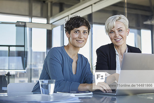 Porträt von zwei lächelnden Geschäftsfrauen mit Laptop am Schreibtisch im Büro