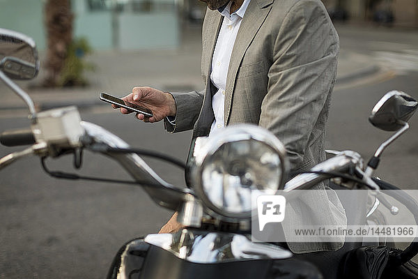 Nahaufnahme eines Geschäftsmannes auf einem Motorroller beim Handy-Check