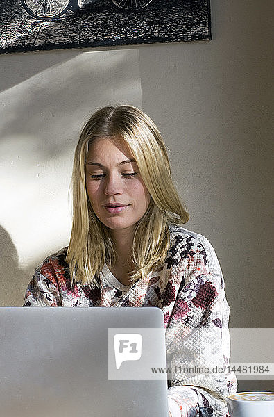Porträt einer blonden Frau  die in einem Café am Laptop arbeitet