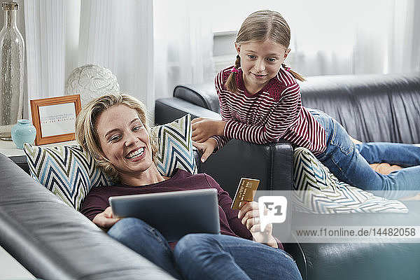 Happy mother and daughter shopping online on couch at home