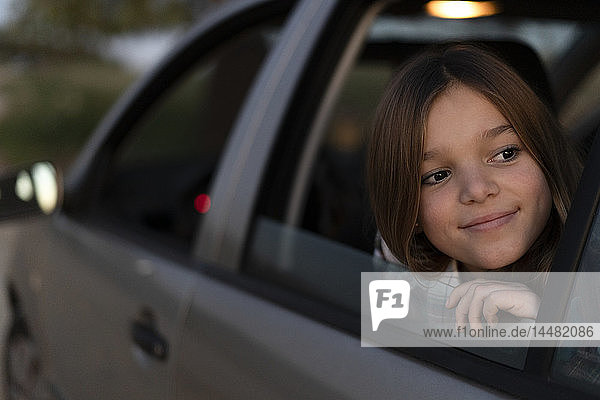 Portrait of content girl looking out of car window in the evening
