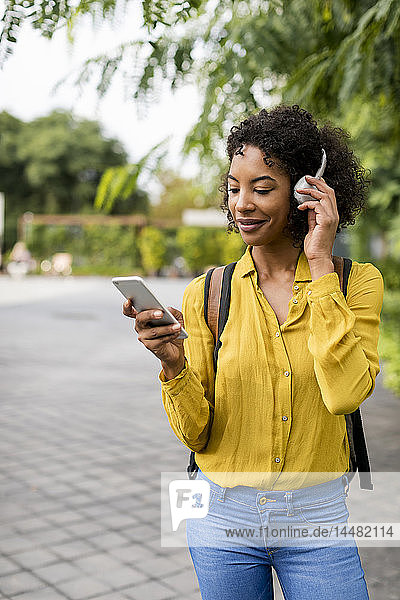Lächelnde Frau  die im Freien mit Kopfhörern und Smartphone Musik hört