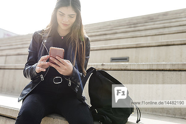Young woman sitting on stairs using cell phone