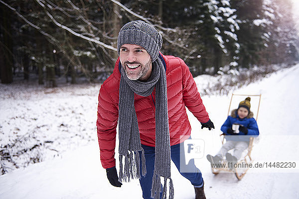 Portrait of smiling father pulling sledge with his son