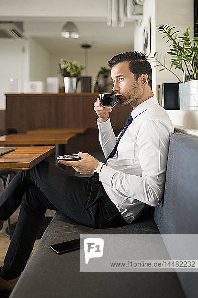 Businessman enjoying coffee and having a break on bench in cafe