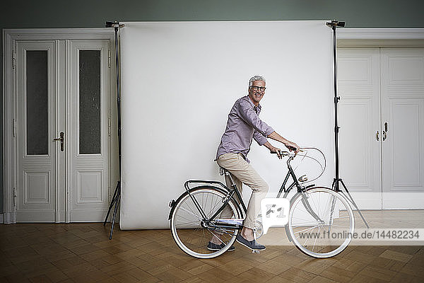 Porträt eines reifen Mannes  der auf einem Fahrrad an einer Projektionswand posiert