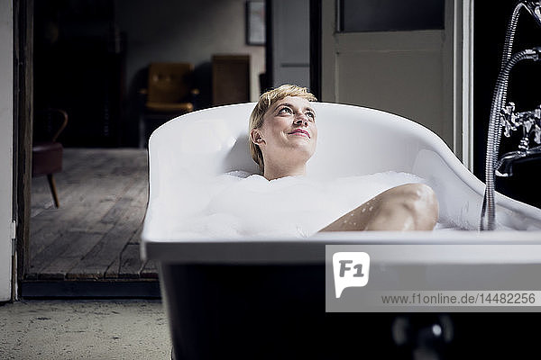 Portrait of happy woman taking bubble bath in a loft