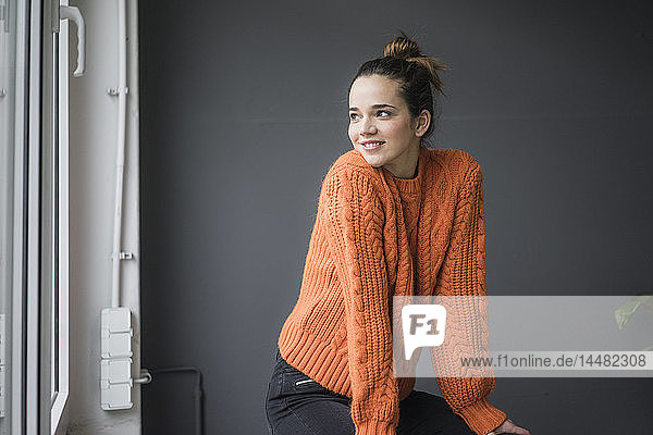 Portrait of smiling woman wearing orange knit pullover looking out of window