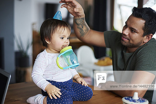 Playful father having fun with his baby sitting on table at home