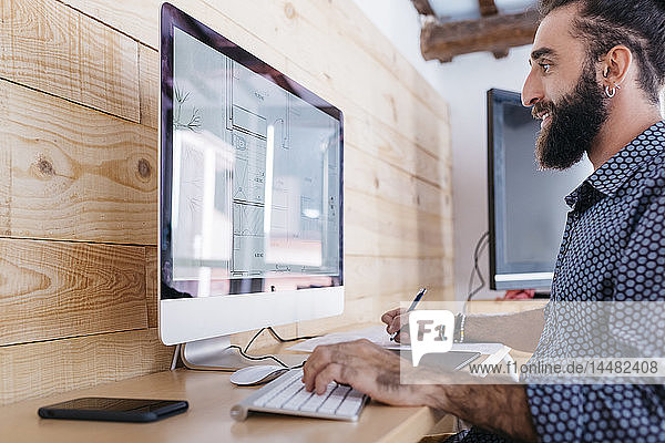 Smiling young man working on floor plan at home using the computer