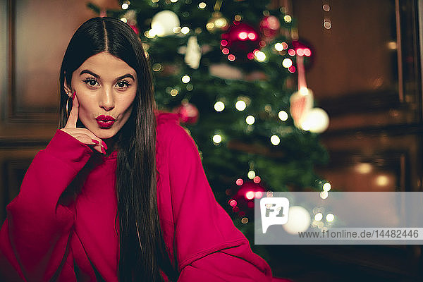 Porträt einer Teenagerin mit Weihnachtsbaum im Hintergrund und schmollendem Mund