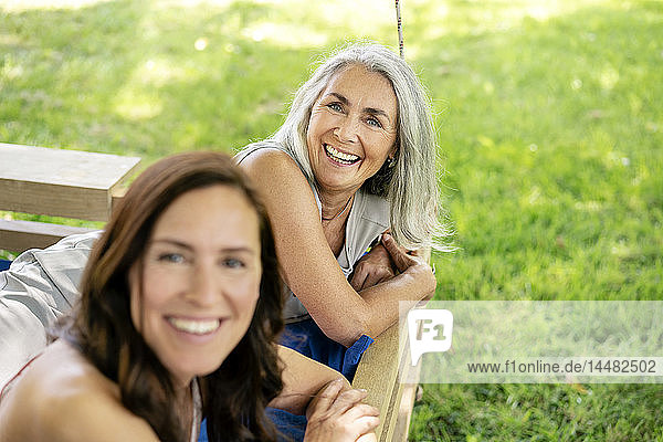 Porträt von zwei glücklichen Frauen  die sich auf einem hängenden Bett im Garten entspannen