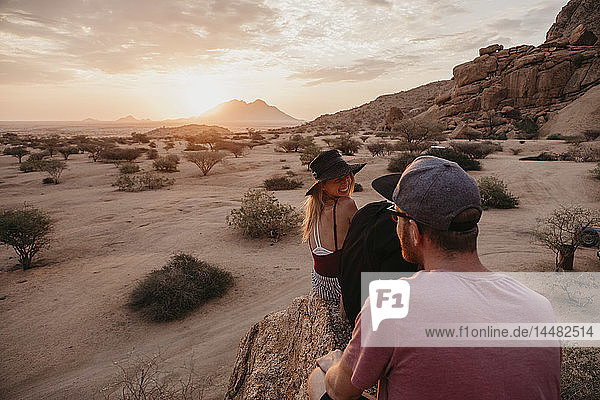Namibia  Spitzkoppe  Freunde sitzen bei Sonnenuntergang auf einem Felsen