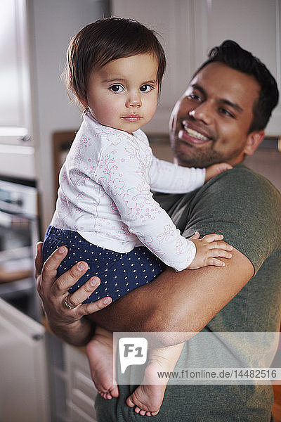 Portrait of smiling father holding baby girl at home