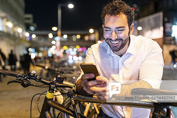 UK  London  glücklicher Mann  der nachts auf sein Telefon schaut