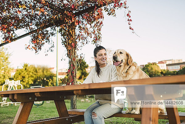 Lächelnde junge Frau mit ihrem Golden-Retriever-Hund  der sich in einem Park ausruht