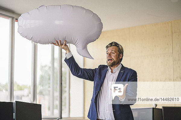 Businessman standing in office  holding inflatable speech bubble