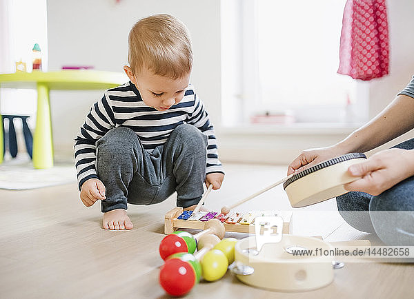 Mother and toddler son playing with musical instruments at home