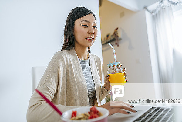 Junge Frau frühstückt  während sie am Laptop arbeitet