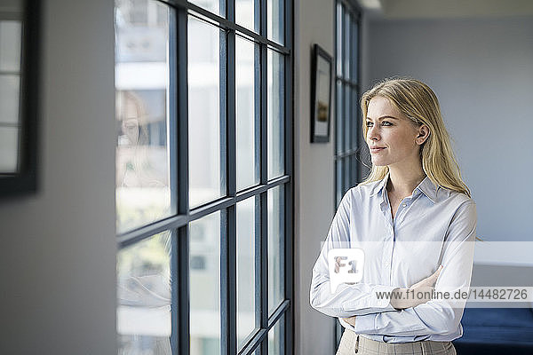 Zuversichtliche Geschäftsfrau steht im Amt und schaut aus dem Fenster