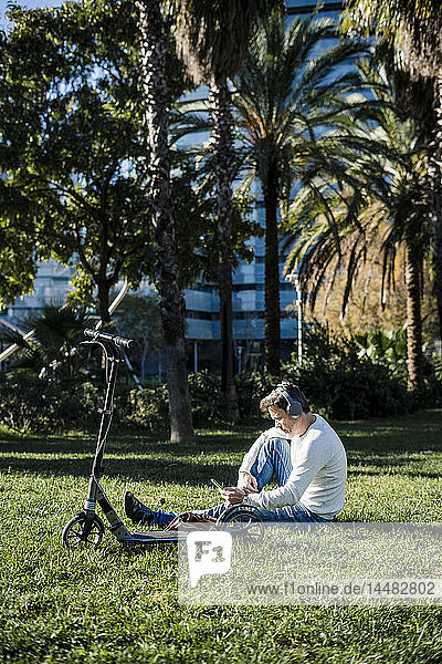 casual businessman sitting on grass in a park  using smartphone and headphones