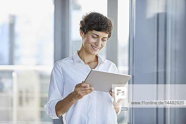 Lächelnde Geschäftsfrau mit Tablette am Fenster im Büro