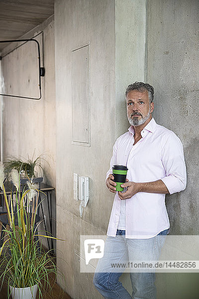 Geschäftsmann hält Kaffeetasse an Betonwand in einem Loft
