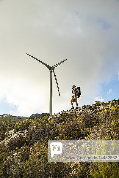 Spanien  Andalusien  Tarifa  Mann auf einer Wanderung auf einem Felsen stehend mit Windrad im Hintergrund
